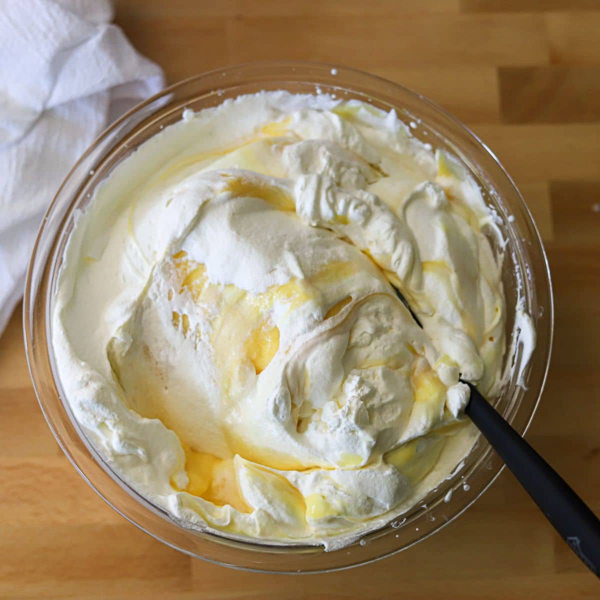 Cool whip being folded into vanilla pudding in a large glass mixing bowl.