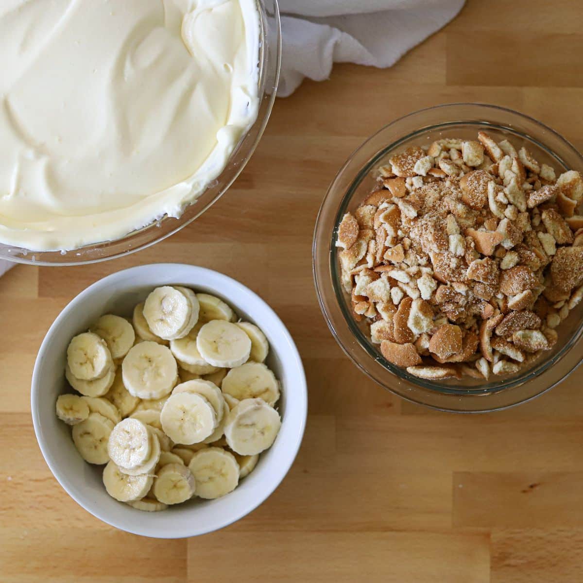 three mixing bowls filled with crushed vanilla wafers, sliced bananas, and vanilla pudding