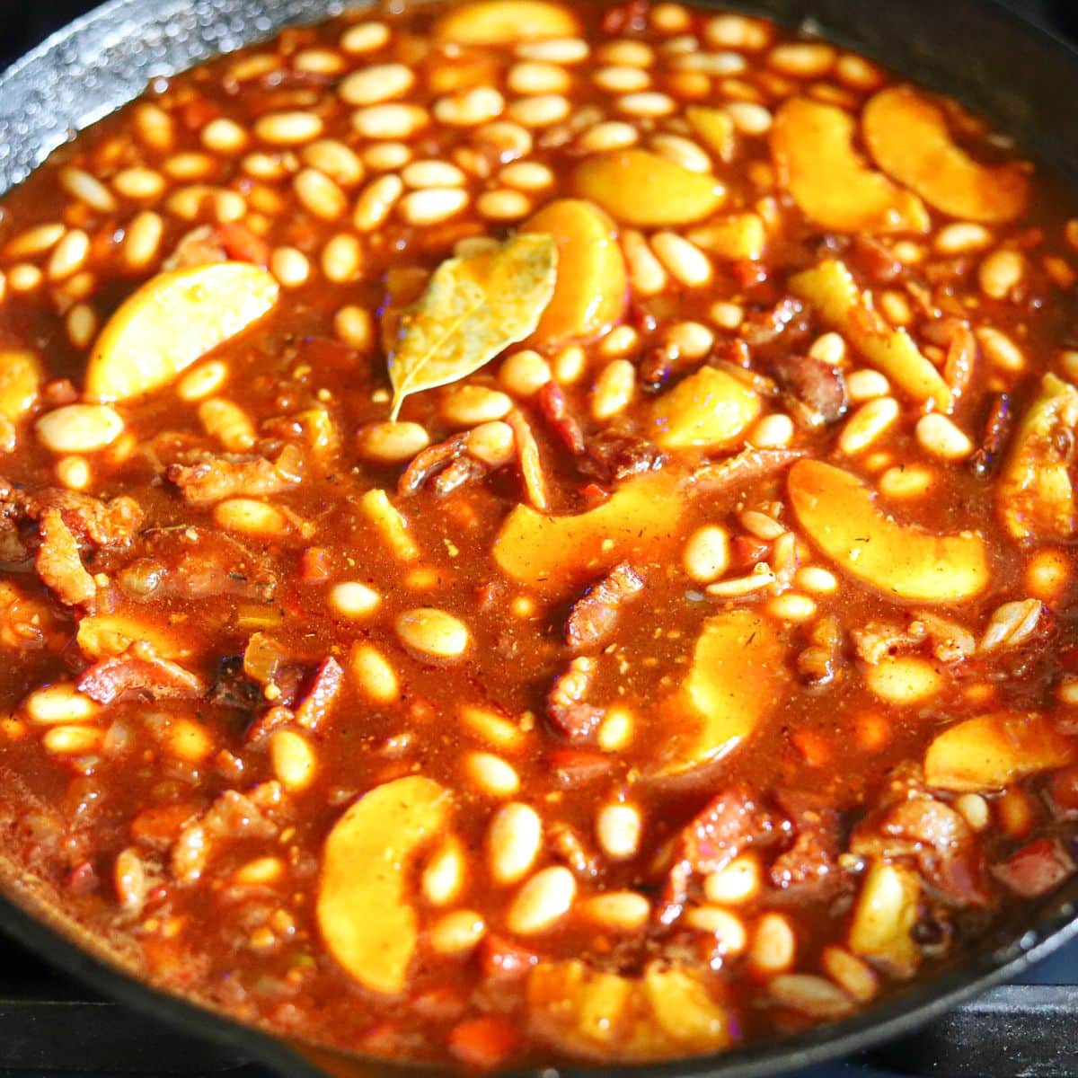 baked beans with peached being prepared in a cast iron skillet.