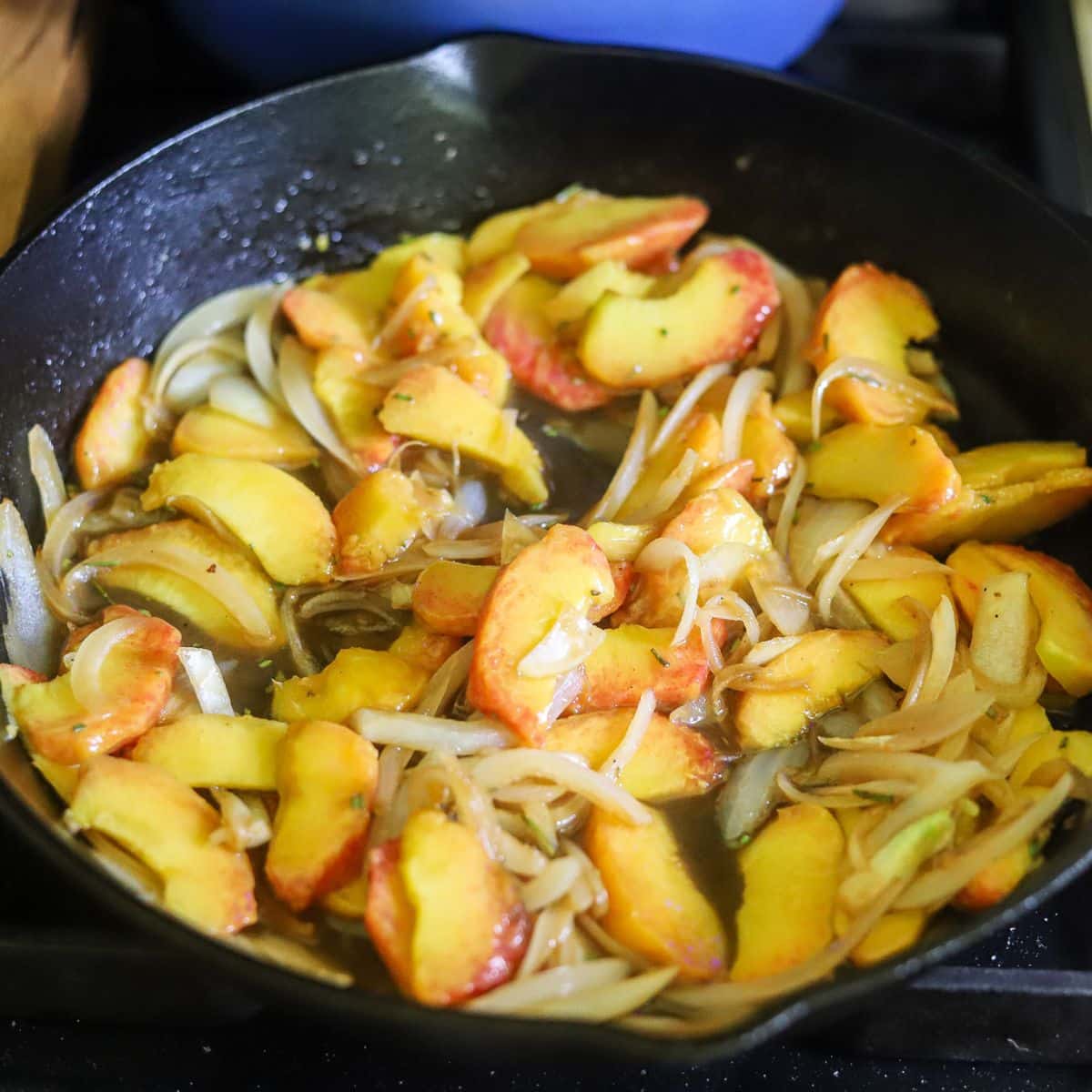 a cast iron skillet filled with fresh sliced peaches, onions, and other seasoning. 